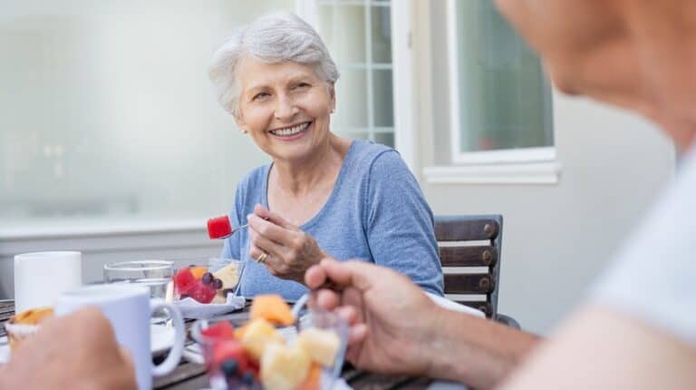 happy senior woman eating fresh fruits during breakfast | Tackle Poor Nutrition and Get Your Senior Eating Healthy With These Yummy Snacks