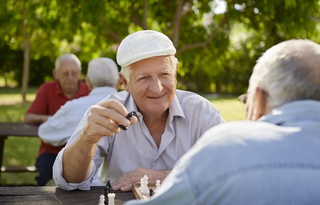 two seniors having fun and playing chess game at park | The Cons of Confinement: Why Seniors Need A Social Life