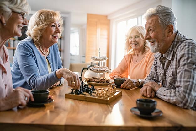 Group of happy seniors communicating while playing boardgame together | 9 Mind Stimulating Activities Great For Seniors