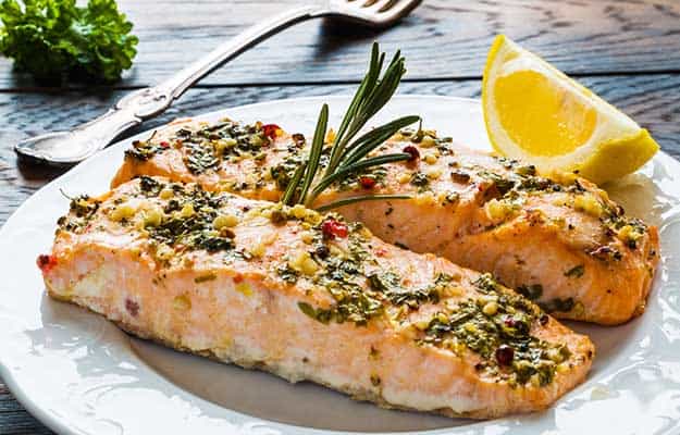 Salmon roasted in an oven with a butter, parsley and garlic. Portion of cooked fish and fresh lemon on a white plate on the wooden table | 9 Hearty And Healthy Dinner Recipes Your Senior Parents Will Love