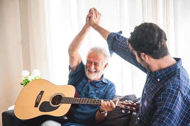 elderly-dad-and-son-are-playing-music-at-home | Senior Conversation Starters: 6 Topics To Talk About With Your Elderly Relatives