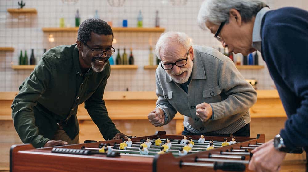 senior friends playing table football | How To Promote Brain Health In Older Adults