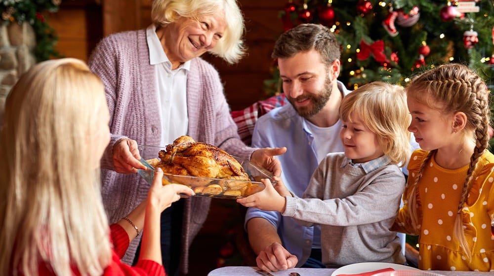12Oaks-grandma bring chicken at table, family sitting by served festive table on Christmas day-ss-Make Christmas Eve Merrier With These 10 Easy _ Appetizing Dinner Meal Ideas-Feature