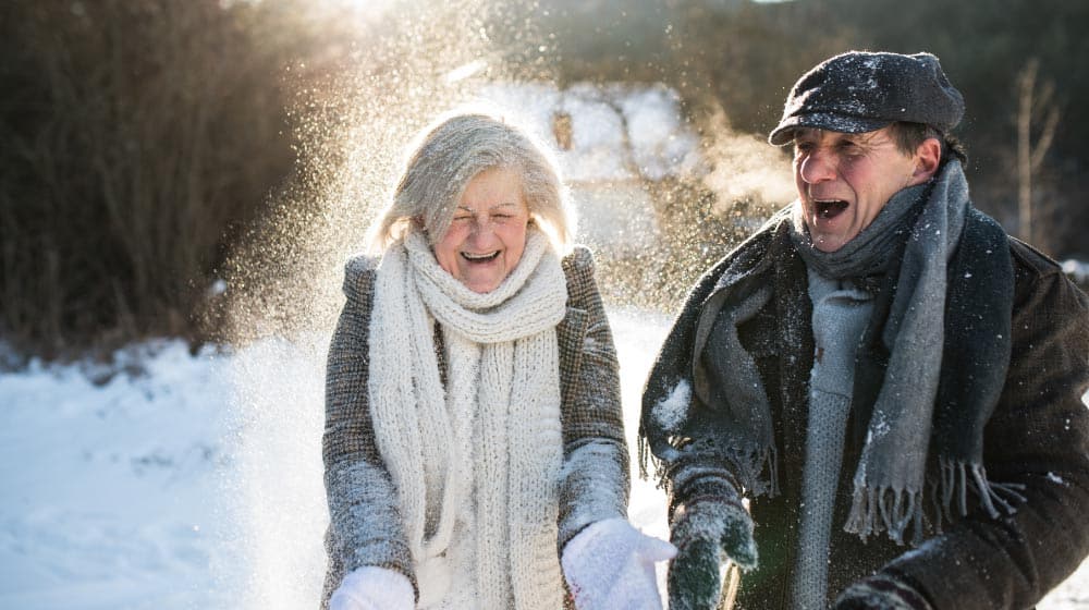 BLOG_12O_senior-couple-blowing-snow_Staying-Safe-This-Winter-Season | feature | 8 Indoor & Outdoor Winter Activities You and Your Older Family Members Will Enjoy
