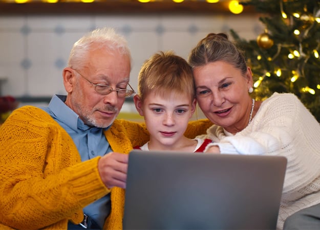 12Oaks-Happy senior couple with grandson choosing christmas movie on laptop-ss-New Year_s Eve Party Theme Nine- Movie Night