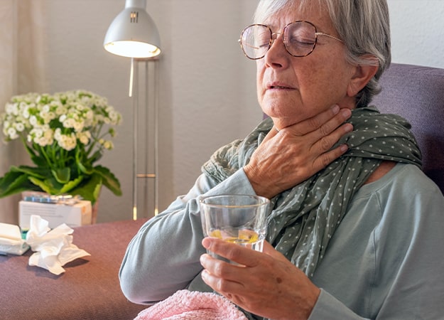 12Oaks-Elderly adult caucasian woman with sore throat and fever as seasonal flu or pollen allergy on sofa at home while drinking glass of water-ss-1.Drink Warm Salt Water for Gargling