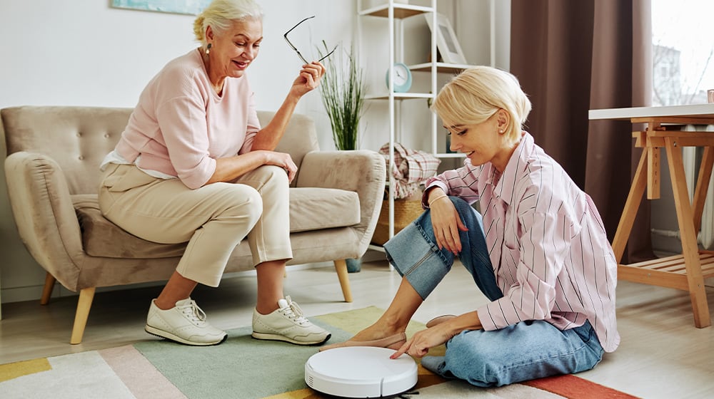 12Oaks-High angle portrait of senior woman using robot vacuum cleaner via smartphone-ss-7 Cool Gadgets That Can Help Seniors in Their Everyday Lives