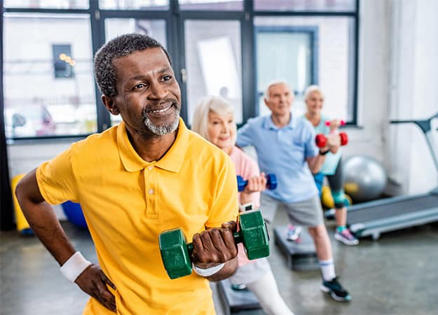 12Oaks-african american man and his friends synchronous exercising with dumbbells at sports hall-ss-Support an Aging Brain at 12 Oaks Communities