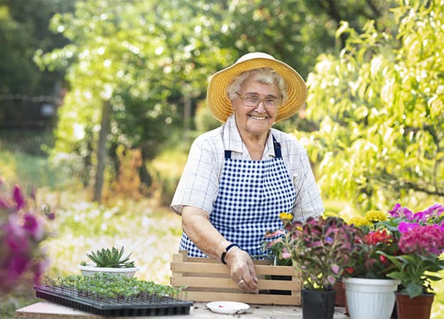 12Oaks-Happy senior woman planting flowers at summer garden-ss-1. Gardening Lowers Stress