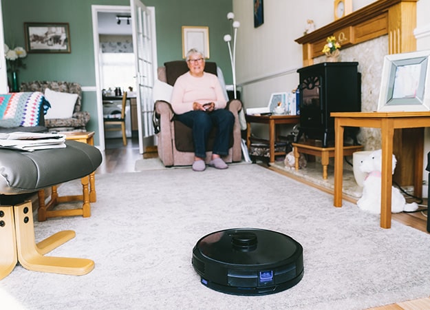 12Oaks-vacuum cleaner robot controlled by senior woman through phone settings while sitting on armchair at home-ss-7. All-At-Once Control of Smart Home Devices