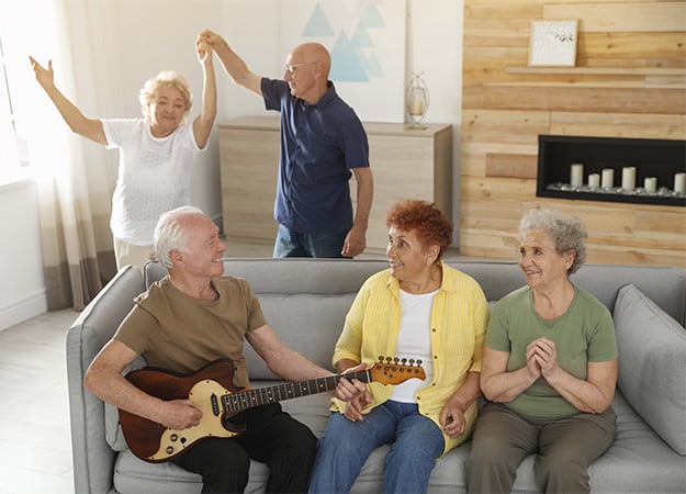 12Oaks-Elderly man playing guitar for his friends in living room-as-How Can 12 Oaks Help Seniors Engage in Music_