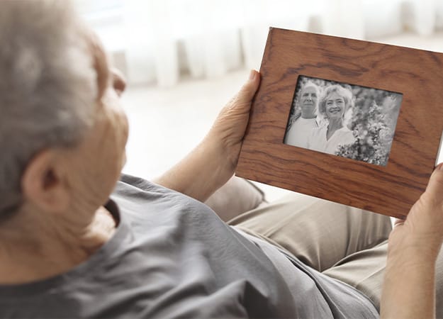 12Oaks-Elderly woman with framed family portrait at home-as-What They May Feel After Losing Their Spouse