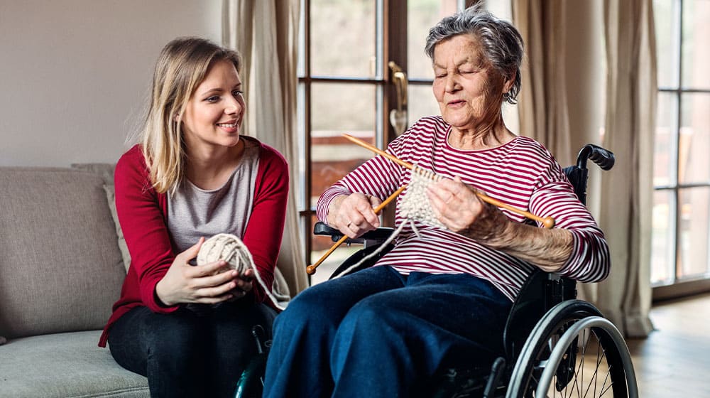 12Oaks-An elderly grandmother in wheelchair with an adult granddaughter knitting at home-as-Interesting Senior Conversation Starters and Icebreakers to Better Communicate With Them-Feature