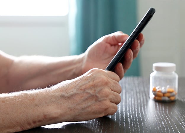 12Oaks-Elderly woman with smartphone and pills sitting at the table-ss-7 Medisafe
