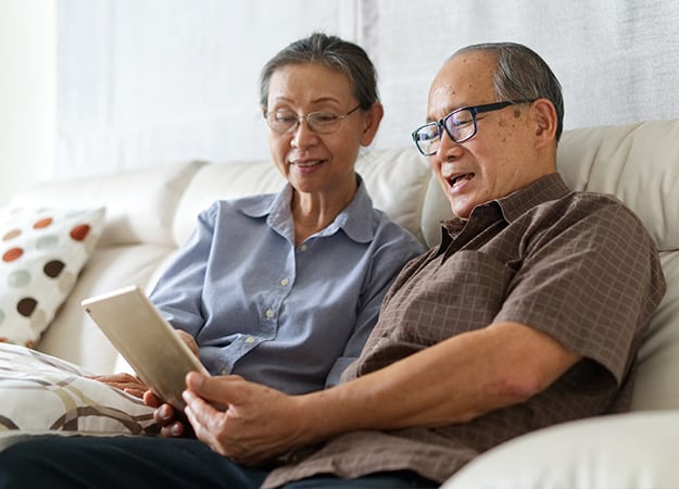 12Oaks-Senior couple sitting on sofa in home playing tablet and relaxing together-ss-5 OurTime