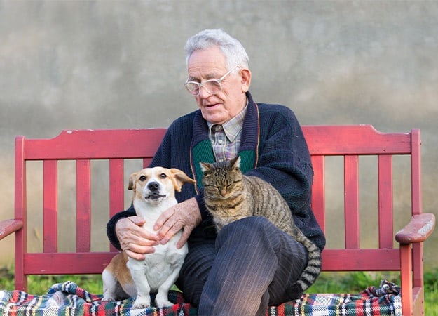 12Oaks-Senior man wirh dog and cat on his lap on bench-as-Tips to Cope with Stress for Seniors
