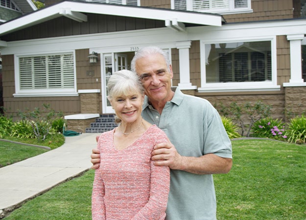 12Oaks-Senior couple standing smiling in front of their home-as-6 State Income Tax Subsidies for Seniors
