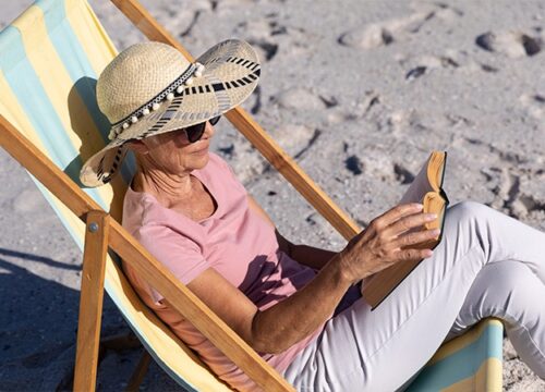 12Oaks-Senior woman sitting on a deck chair and reading at the beach-as-3 Soak up the Sun