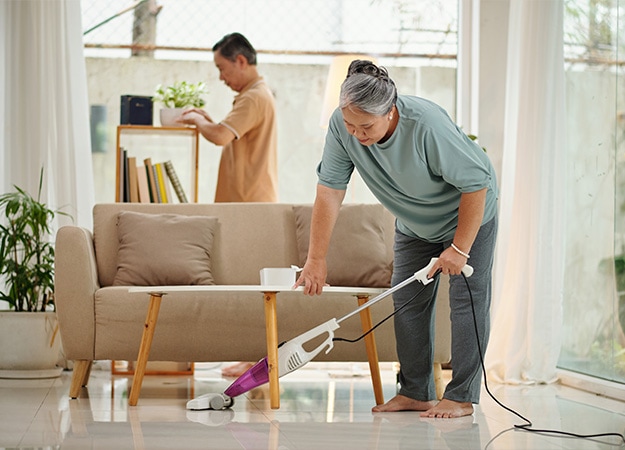 12Oaks-Senior woman vacuum cleaning floor when husband wiping dust-as-2 Doing Home Chores