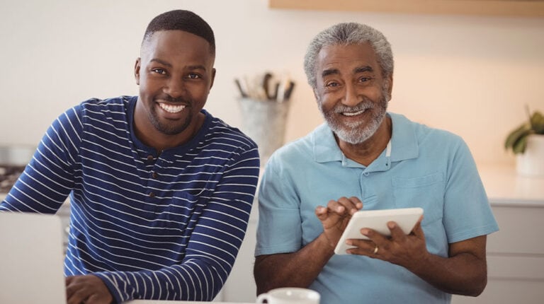 12Oaks-Smiling father and son using laptop and digital tablet in kitchen-as-How to Use the AARP Retirement Calculator-Feature