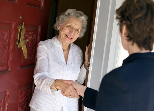 12Oaks-Smiling senior woman greeting visitor at the front door-as-7 Selling A House