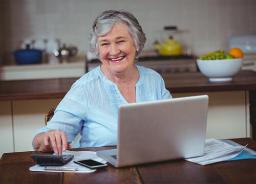 12Oaks-Smiling senior woman using calculator and laptop-as-How to Use the AARP Retirement Calculator