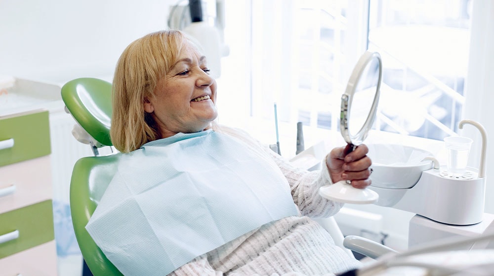 12Oaks-Elderly woman looking at her teeth in a mirror-pexels-The Importance Of Dental Care For Our Elderly Loved Ones-Feature