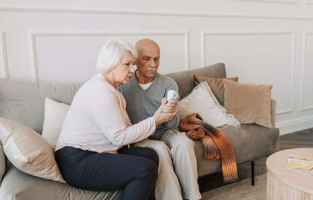 Elderly-Man-and-Woman-Sitting-on-Couch-Using-a-Digital-Thermometer-Prevents-Diseases