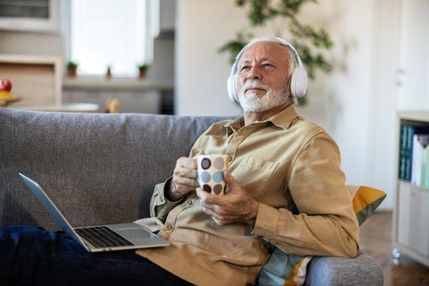 Elderly man on a sofa holding a mobile phone and listening to music on headphones