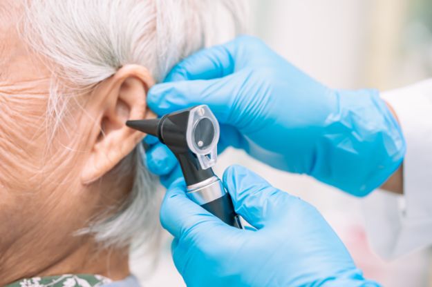 Audiologist or ENT doctor use otoscope checking ear of asian senior woman patient treating hearing loss problem