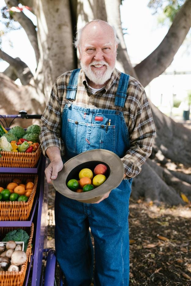 Man with Gray Beard Holding a Hat full of Colorful Fruits