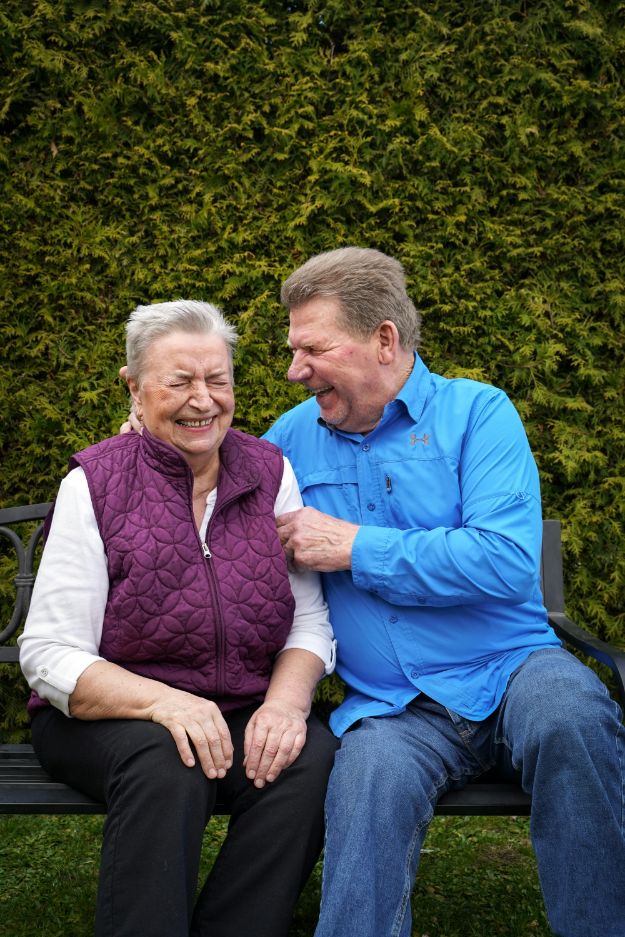 Senior Couple Sitting on a Bench by a Hedge, and Laughing 
