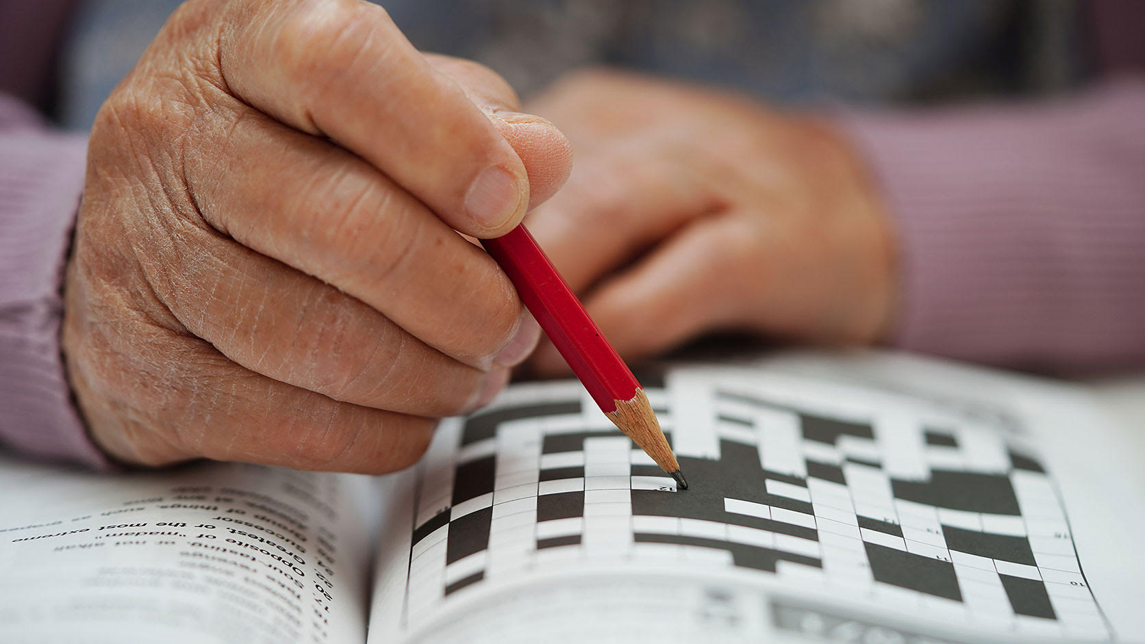 Close-up of an older person filling out a crossword puzzle with a red pencil